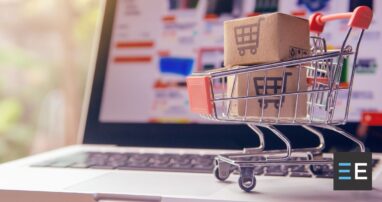 A miniature shopping cart with two boxes in it placed on a laptop