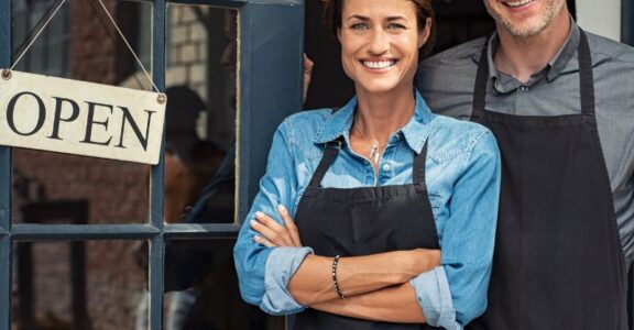 Two people smiling next to an open sign